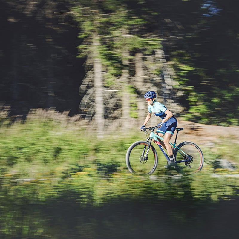 Eine Person fährt im Wald mit einem Cube Access Women Series Mountainbike.