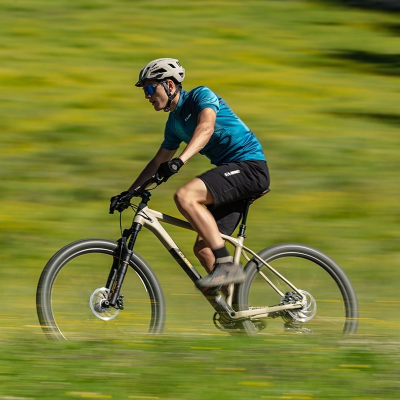 Mann auf Cube Reaction Mountainbike fährt mit Helm und Sportkleidung über grüne Wiese.