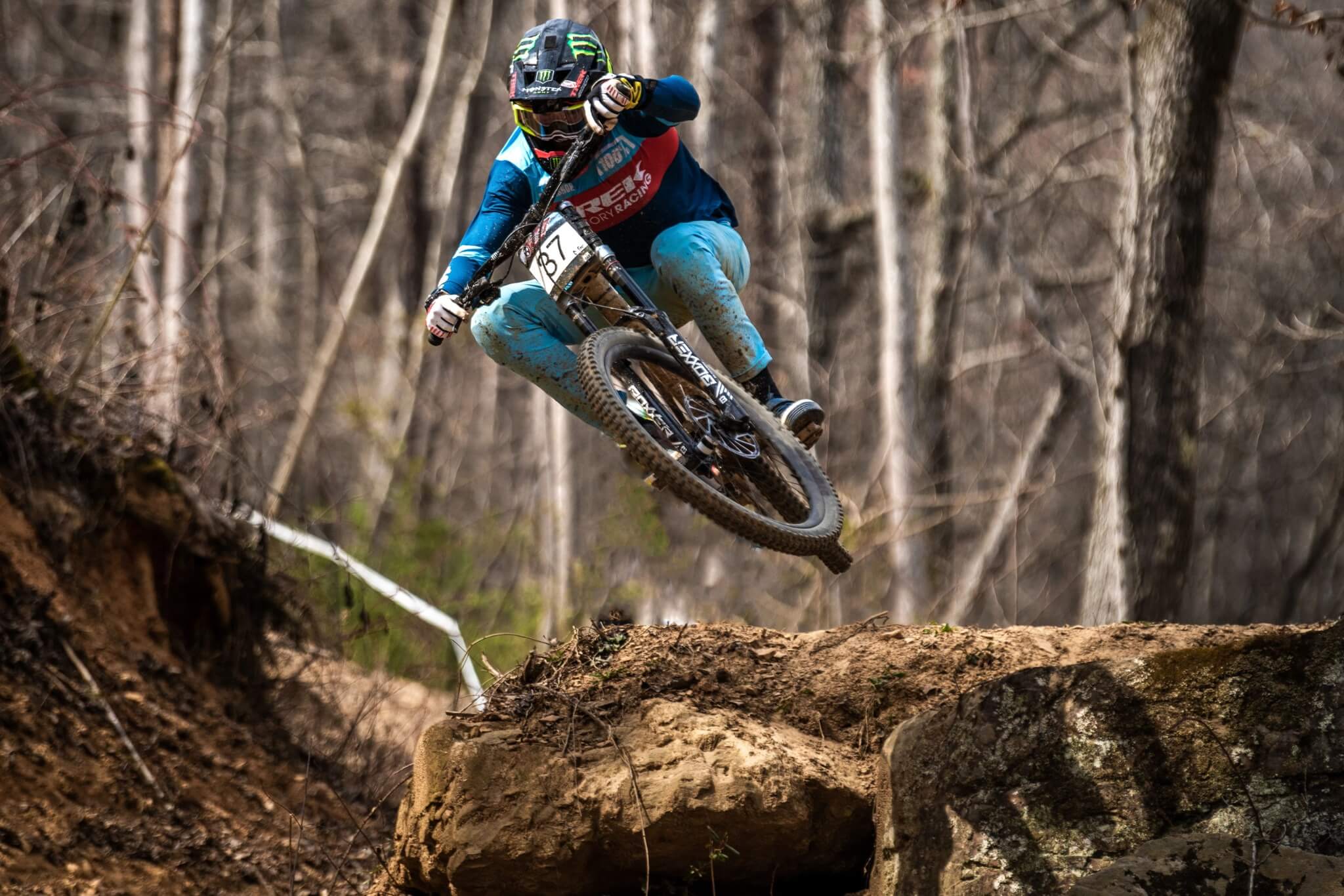 Mountainbiker springt mit einem Trek Session Bike über einen Felsen im Wald. Actionreiche Downhill-Szene.