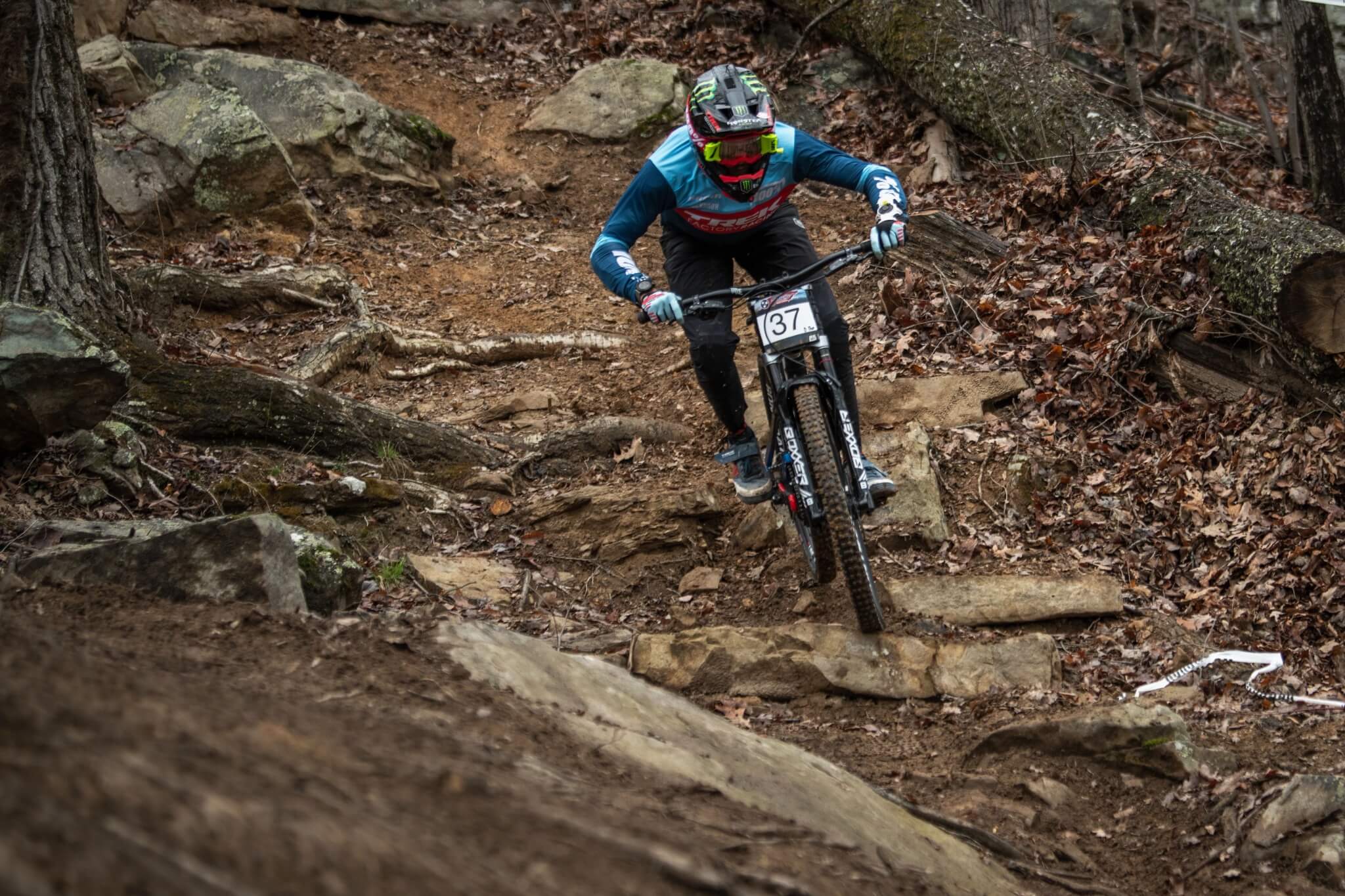 Mountainbiker auf steinigem Trail mit einem Downhill-Bike in Aktion, trägt Schutzausrüstung.