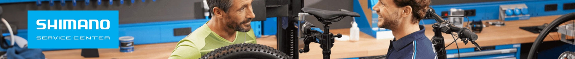 Shimano Service Center: Zwei Männer reparieren Fahrräder in einer Werkstatt mit blauer Einrichtung.