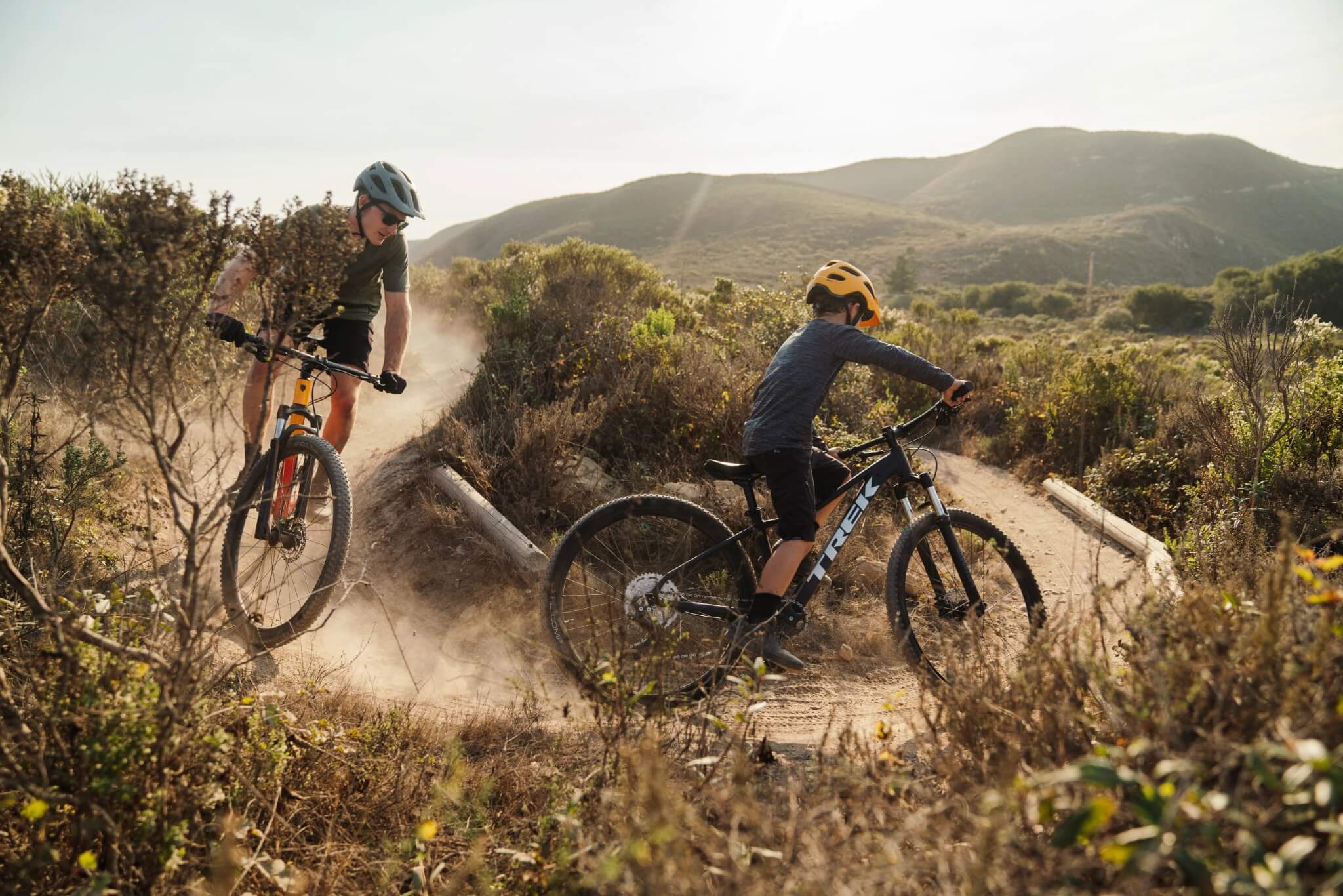 Zwei Personen fahren Trek Marlin Mountainbikes auf einem staubigen Trail durch eine hügelige Landschaft.