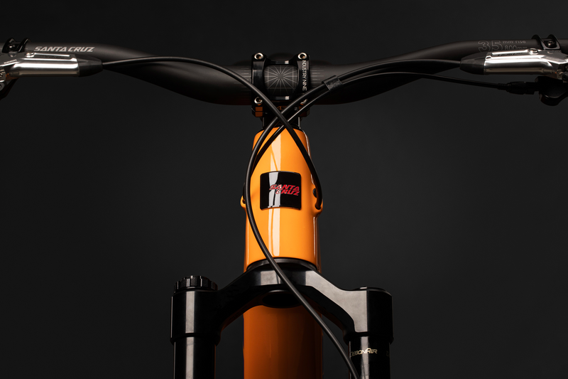 Santa Cruz Tallboy Mountainbike-Co-Rahmen in Orange, Fokus auf Vorderseite und Lenkstange vor dunklem Hintergrund.
