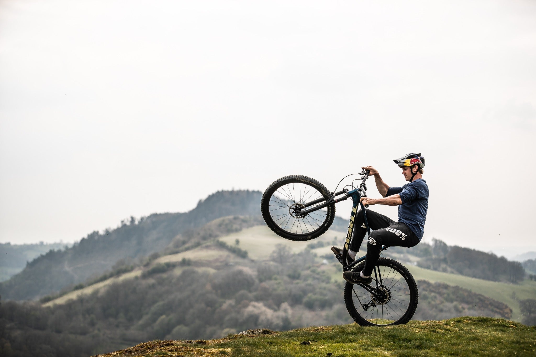 Person macht Wheelie auf Mountainbike Trek Roscoe vor hügeliger Landschaft.