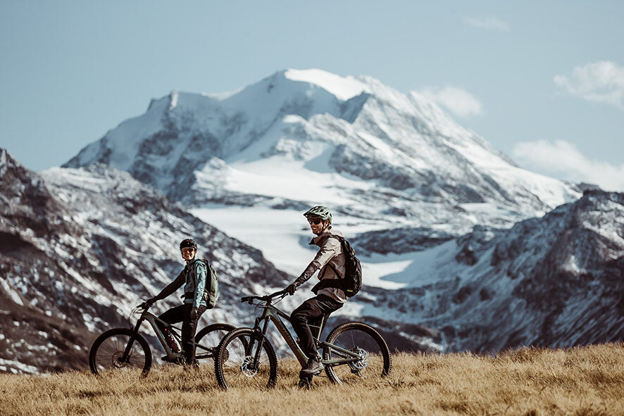 Zwei Personen auf Specialized E-Bikes vor schneebedecktem Berg, ideal für Mountainbike-Touren in alpiner Umgebung.