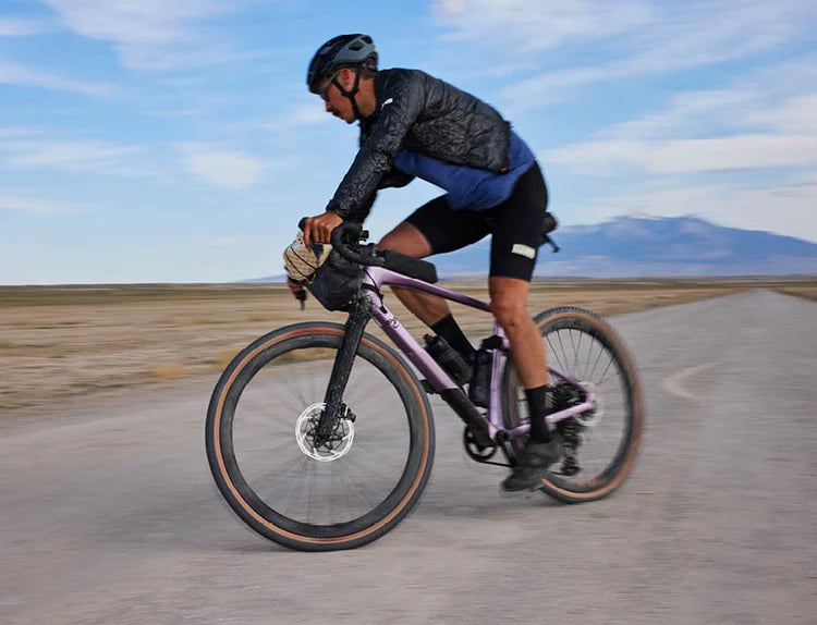 Person fährt ein lila Gravel-Bike auf einer Straße, geeignet für Abenteuertouren.