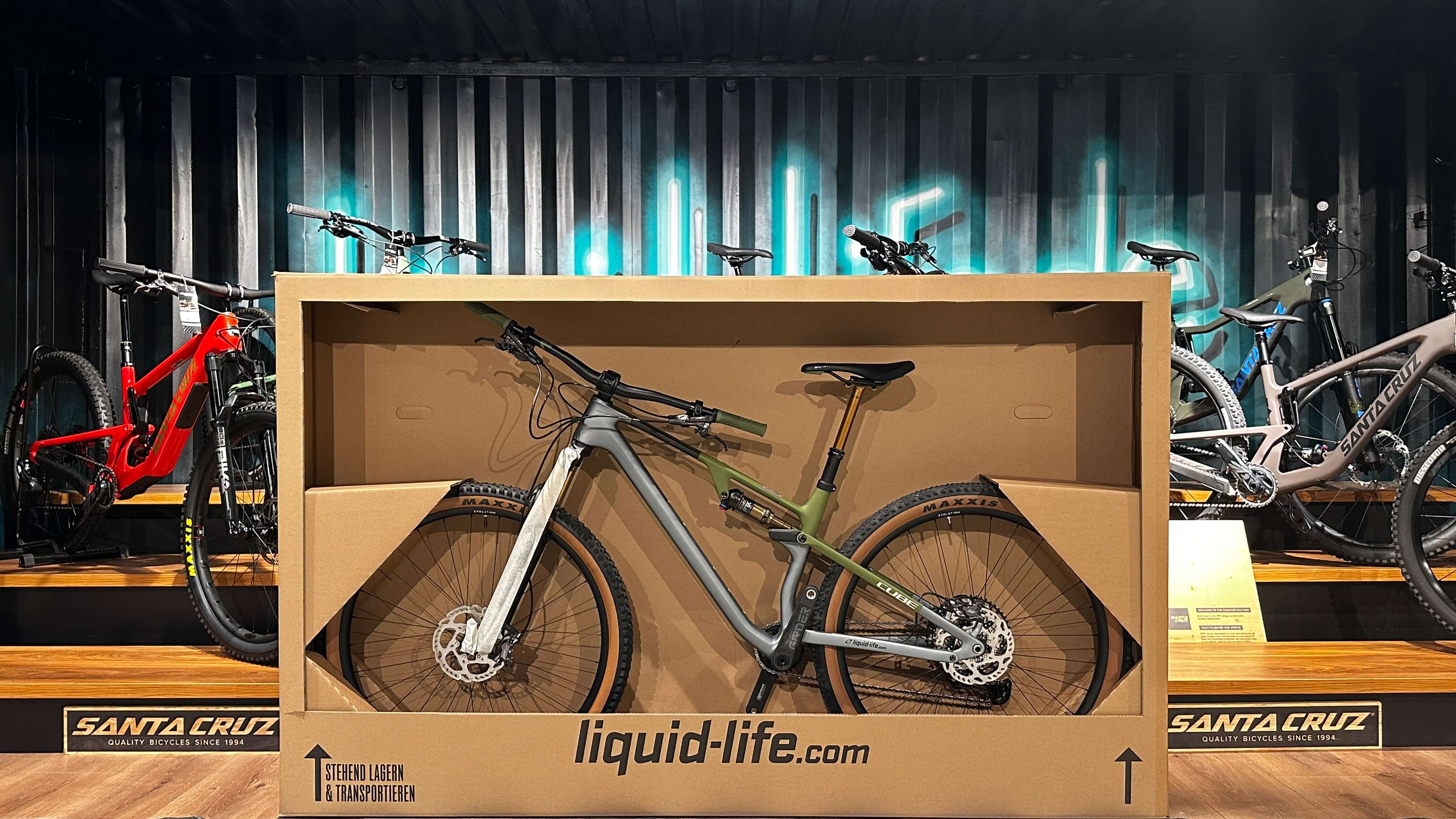 Mountainbike in grauer Box, Marke Cube, auf Holzpodest in Fahrradgeschäft, Hintergrund mit weiteren Bikes.