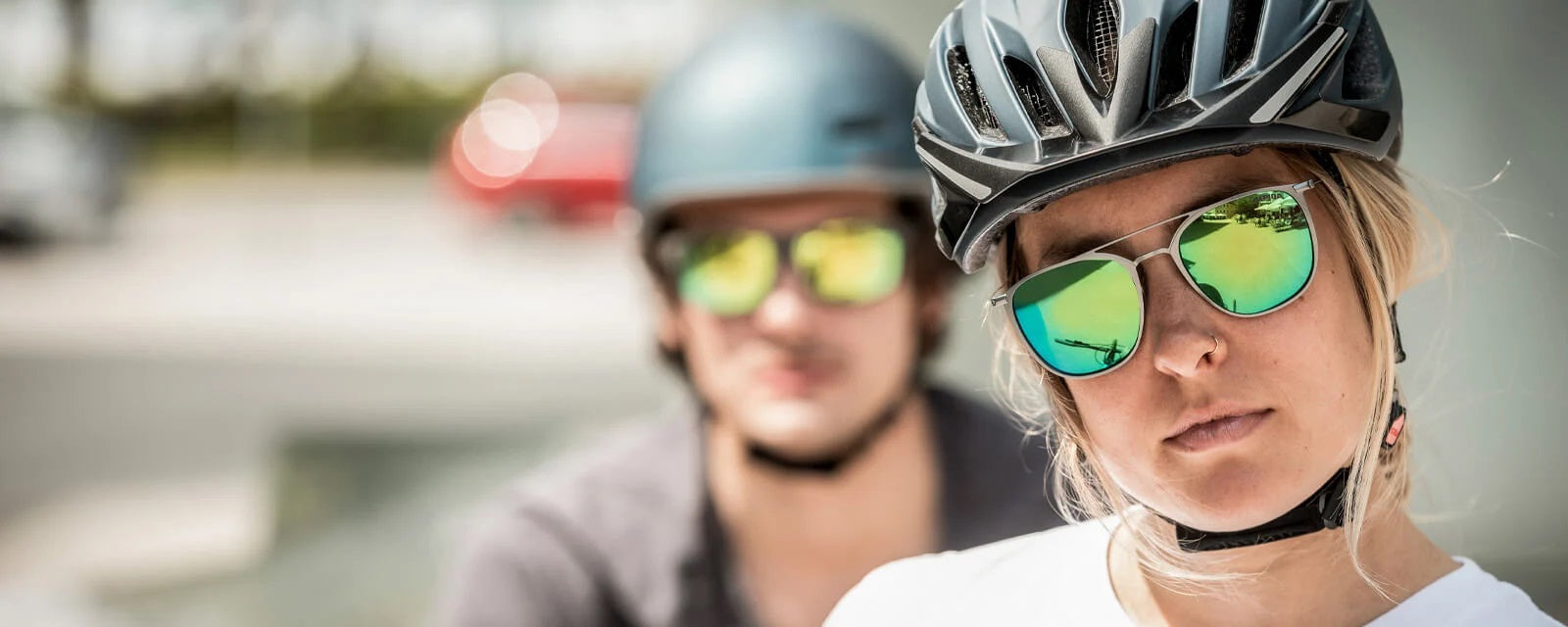 Zwei Personen mit Radhelmen und verspiegelten Sonnenbrillen, die entspannt in die Kamera schauen.