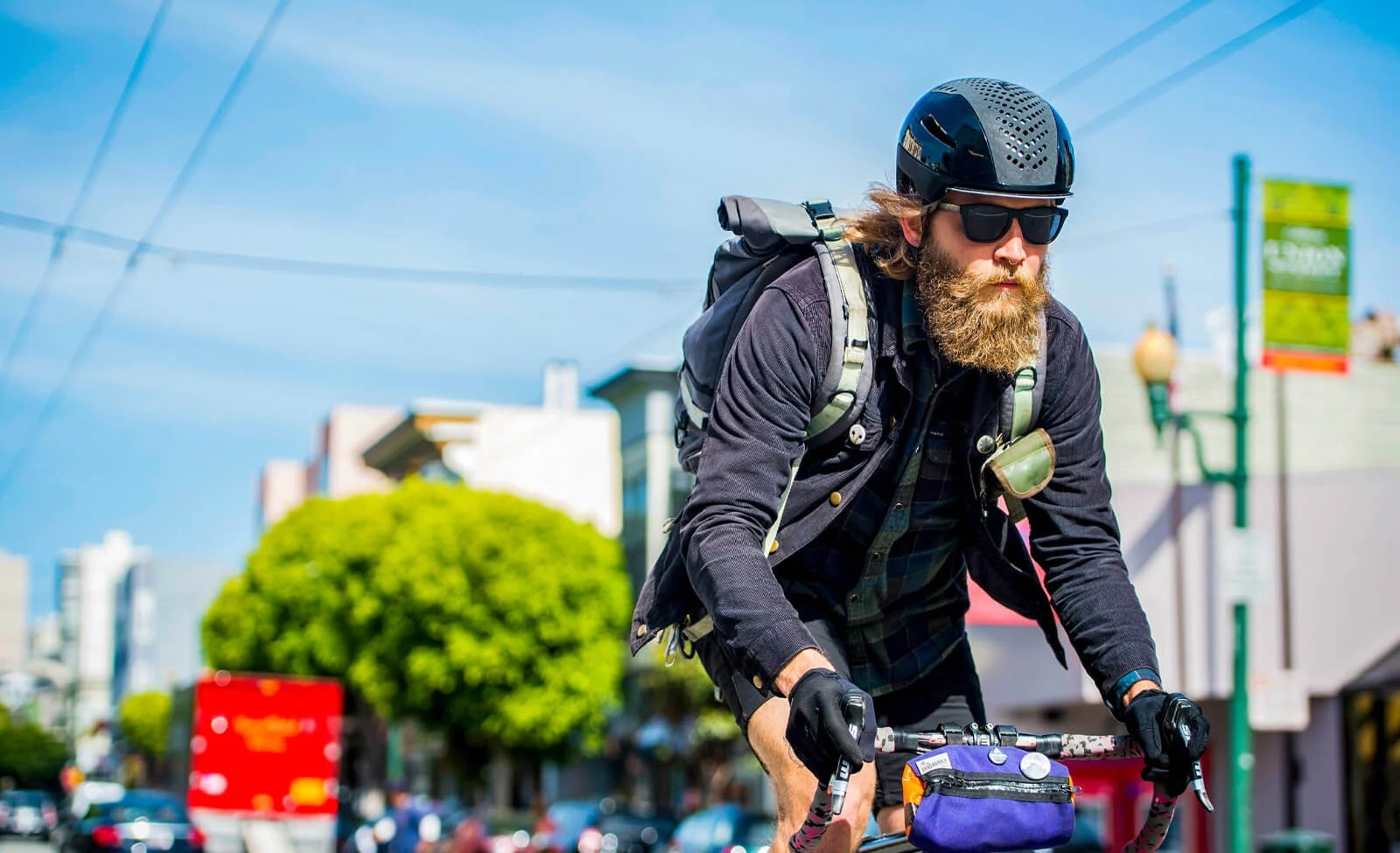 Radfahrer in der Stadt, trägt Helm und Sonnenbrille, mit Rucksack und Fahrradtasche. Urbaner Stil, sportlich und aktiv.