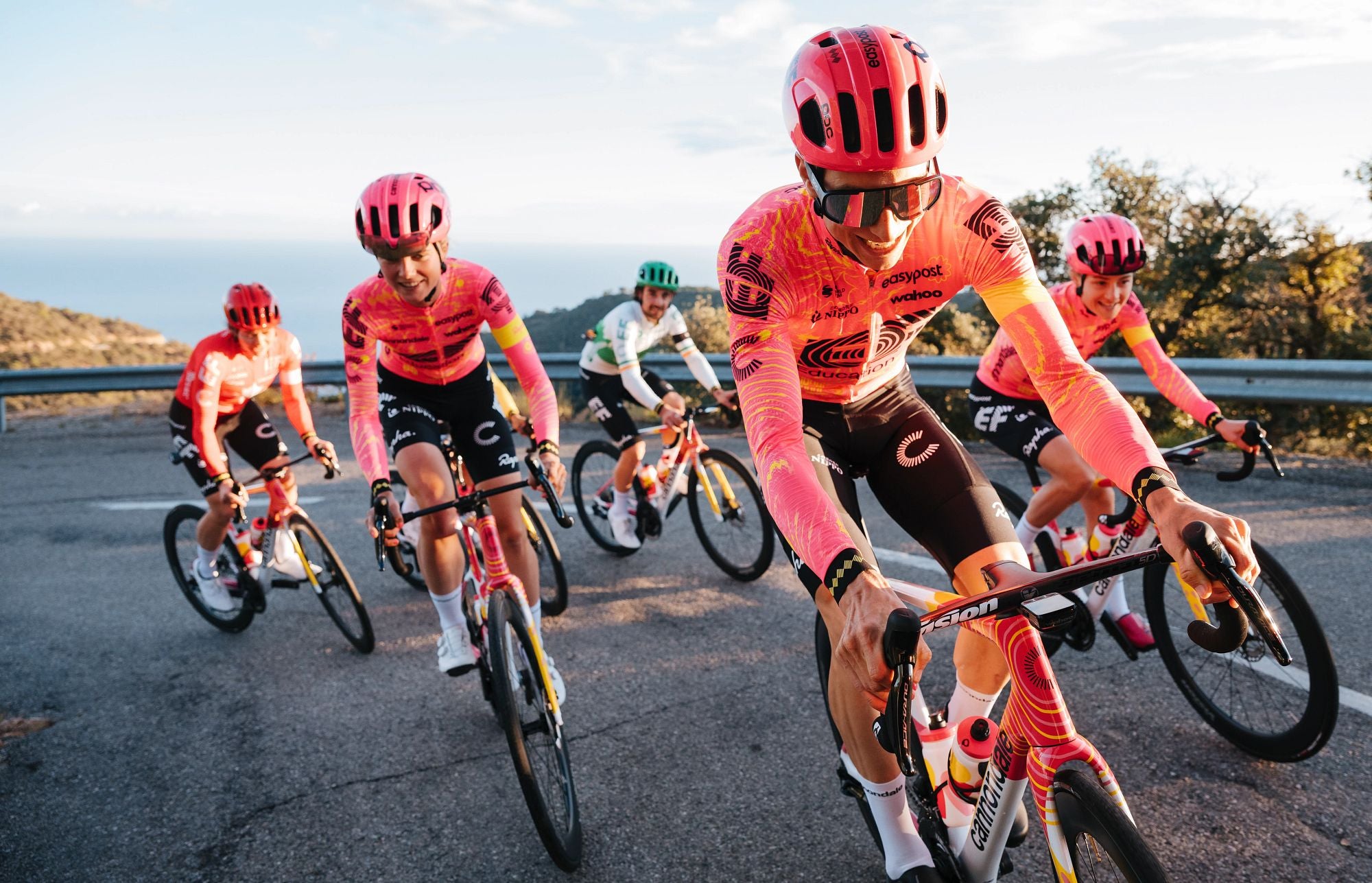 Radrennfahrer in pinken Trikots auf Cannondale-Rennrädern in einer Hügelkurve.