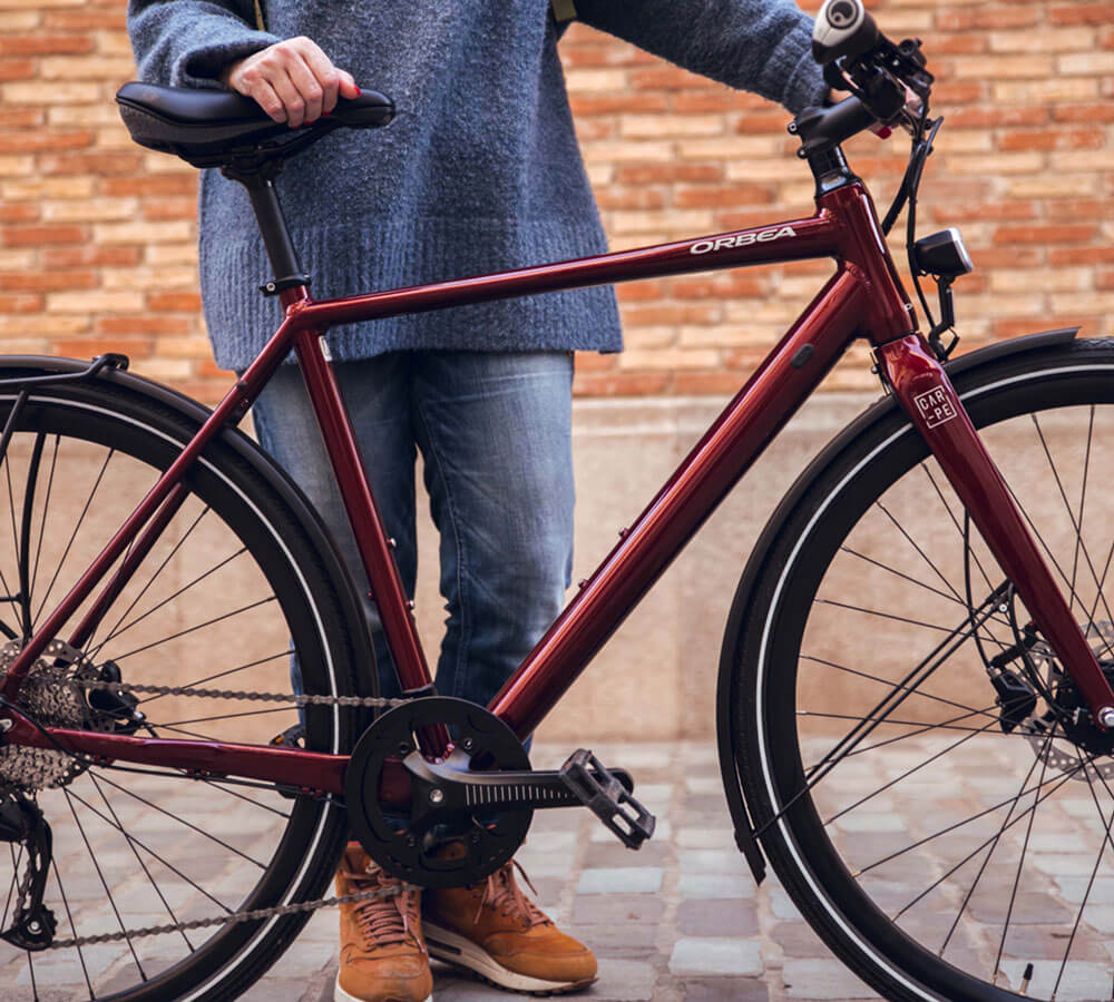 Rotes Orbea Carpe Fahrrad, lehnend an Person, geeignet für Stadtfahrten.