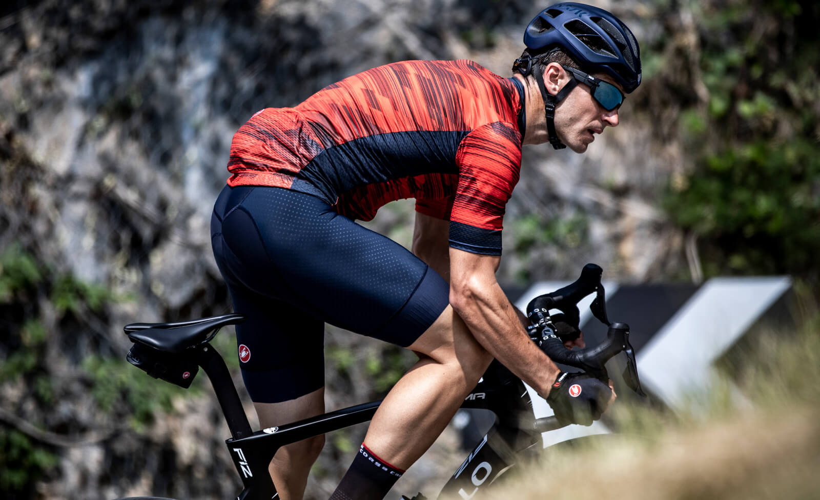 Radfahrer in rotem Castelli-Radtrikot und schwarzer Hose, fährt Rennrad bergauf, Zielgruppe: Rennradfahrer.