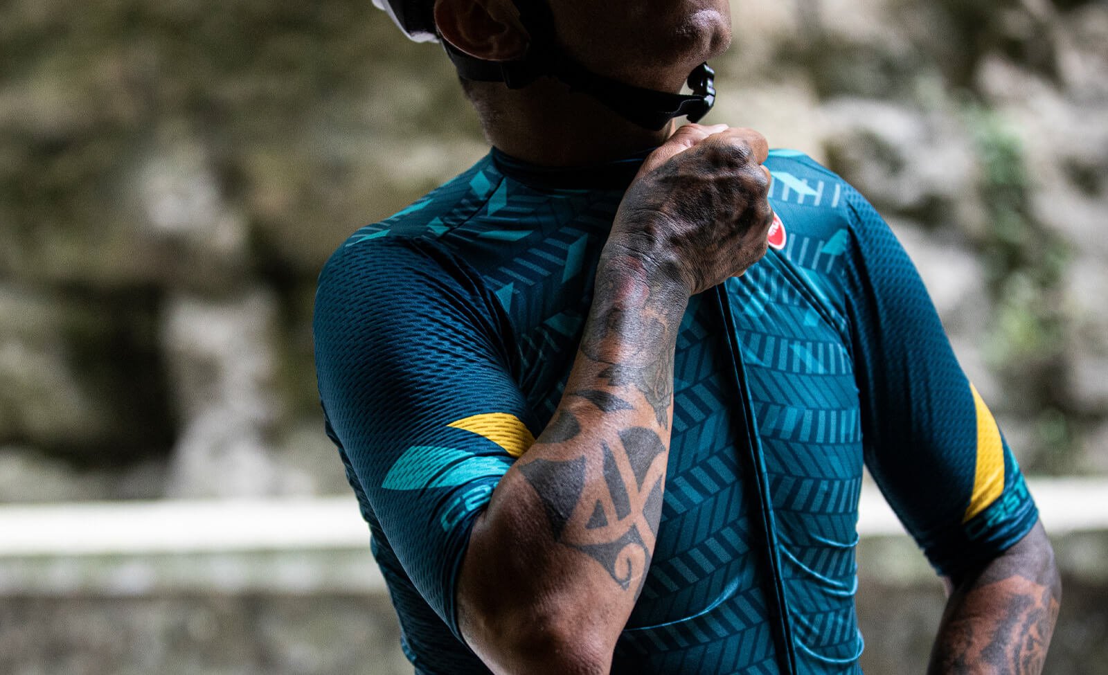 Radfahrer in blau-gelbem Castelli-Radtrikot richtet seinen Helm; geeignet für Radsport und Outdoor-Enthusiasten.