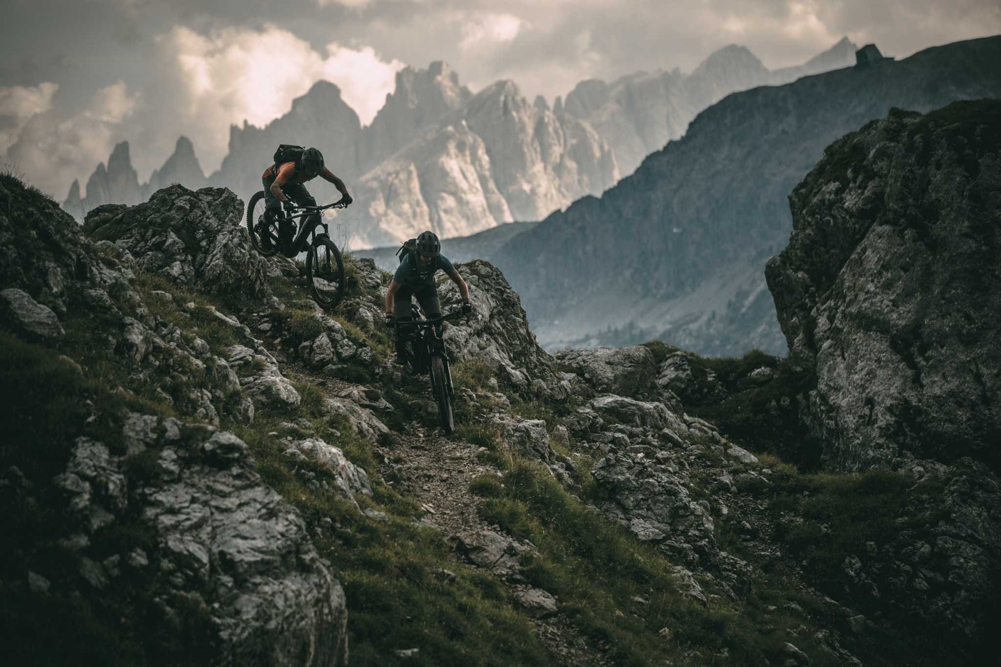 Zwei Mountainbiker fahren mit Trek Rail Mountainbikes in felsigem, alpinem Gelände bei bewölktem Himmel.