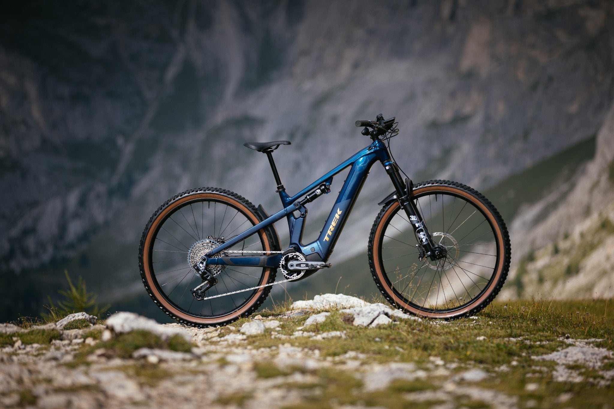 Trek Powerfly FS E-Mountainbike, blau, auf felsigem Untergrund vor Bergkulisse, ideal für Gelände und Abenteuer.