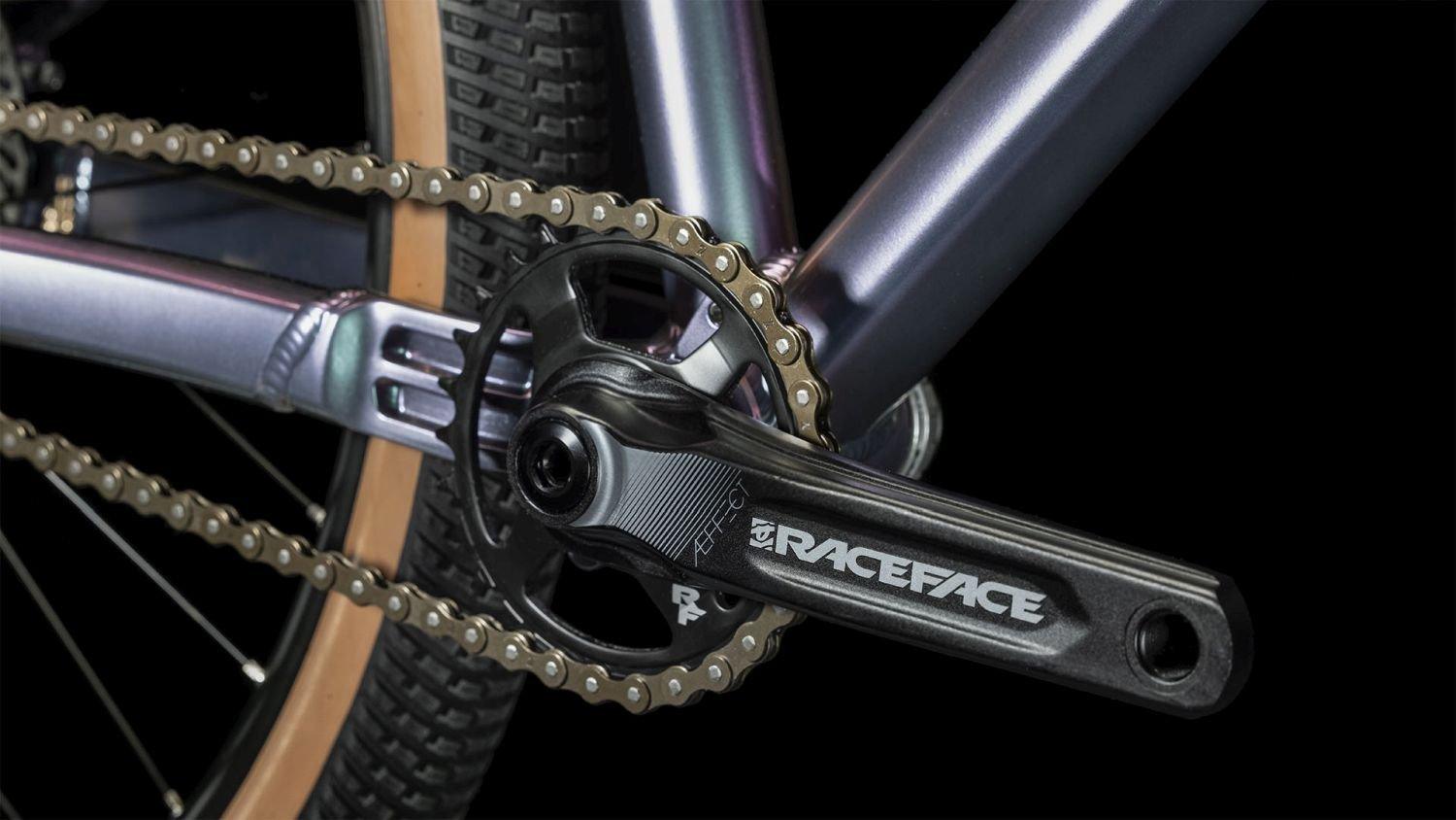 Nahaufnahme eines Fahrradkurbelarms von RaceFace mit Kette und Teil eines Reifens, geeignet für Offroad-Fahrräder.