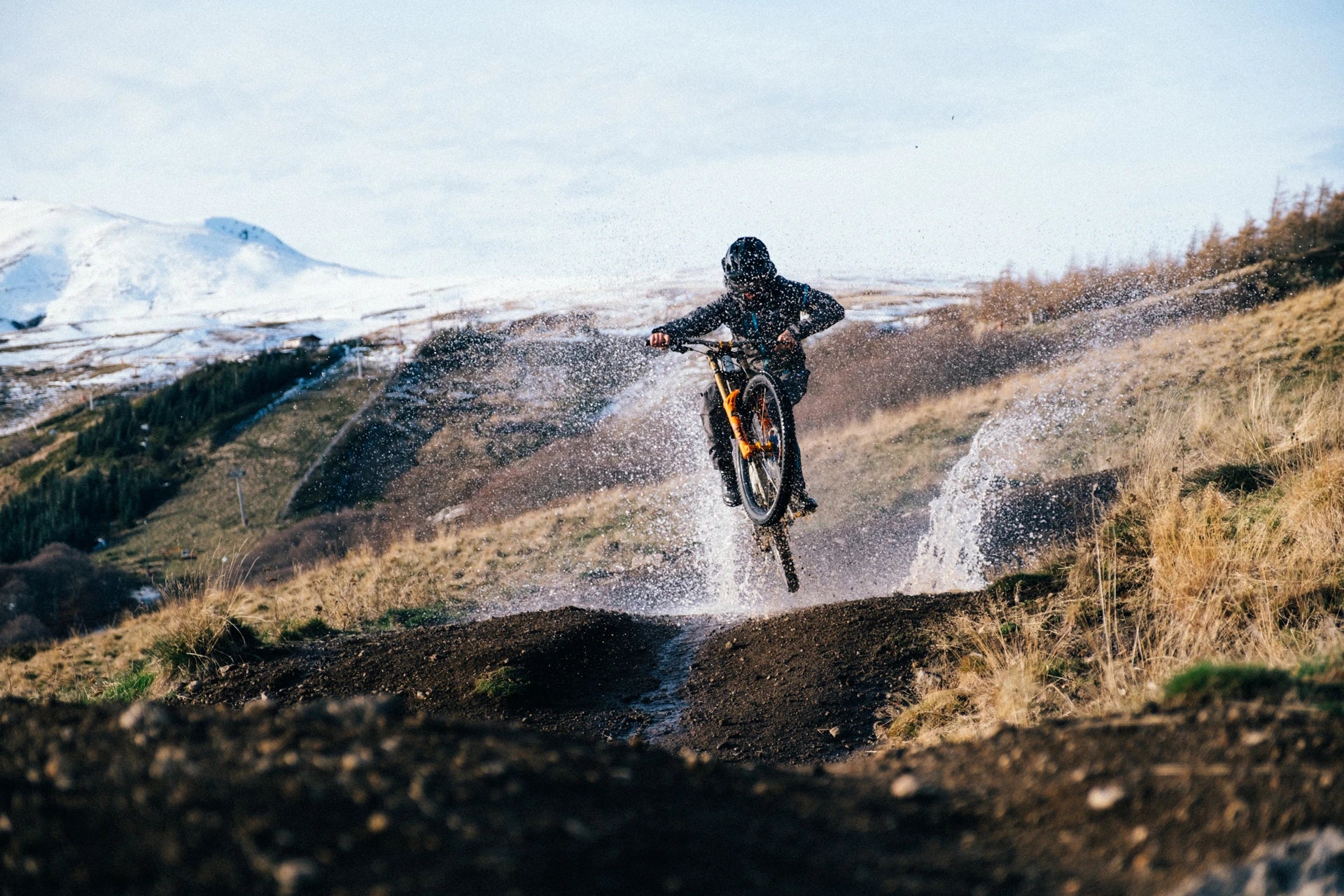 Mountainbiker springt über matschige Pfütze in hügeliger Landschaft, ideal für Outdoor-Abenteuer.