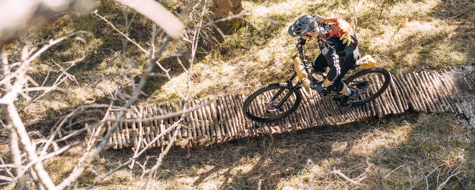 Mountainbiker auf schmalem Holzpfad im Wald, trägt Helm und Rucksack. Abenteuersport im Freien.