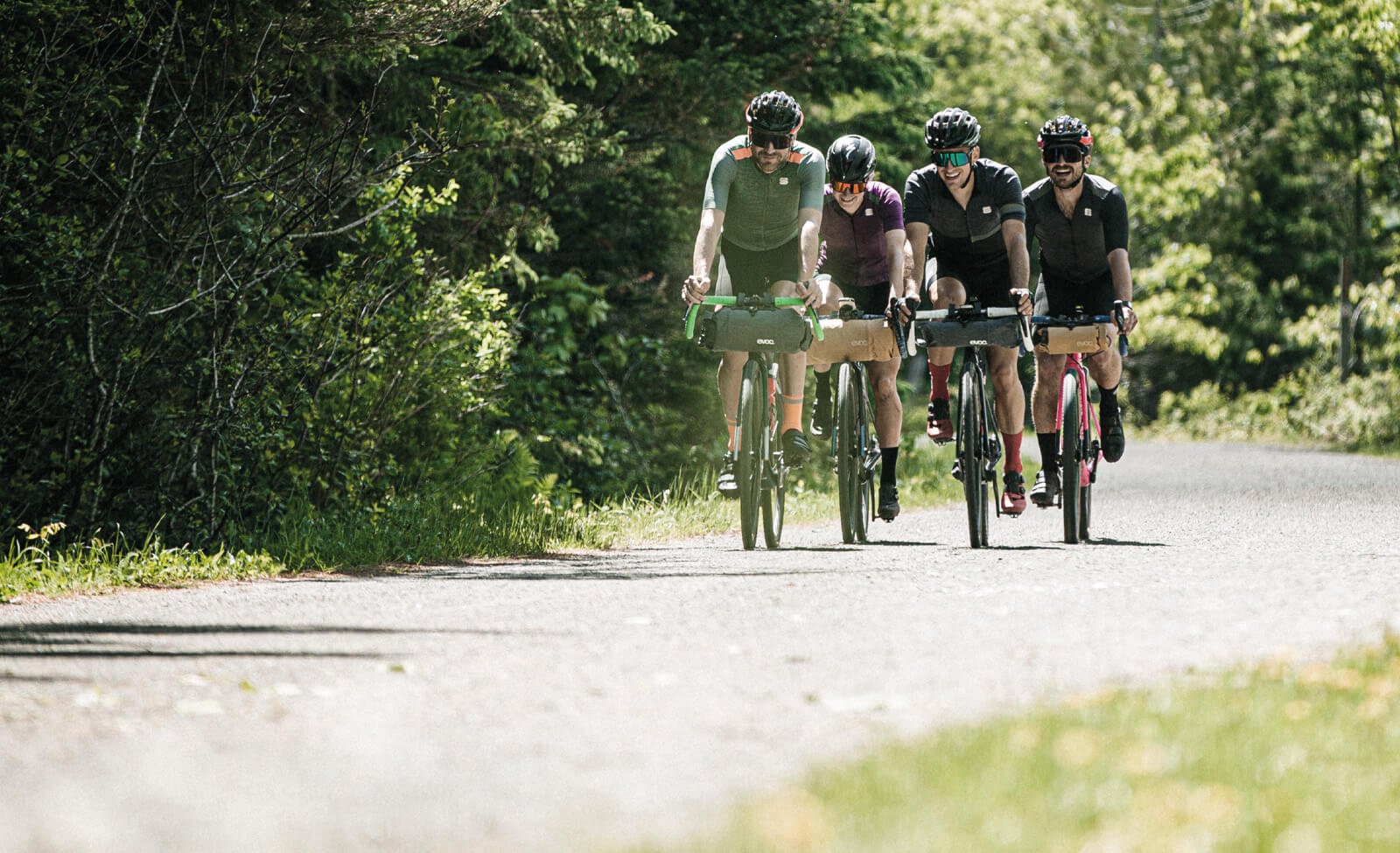 Gruppe Radfahrer mit Evoc-Taschen auf einer Straße in ländlicher Umgebung, ideal für Outdoor-Abenteuer.