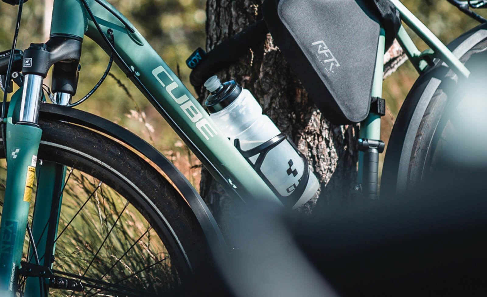 Grünes Cube Fahrrad mit Trinkflasche und RV-Tasche neben einem Baum im Freien.