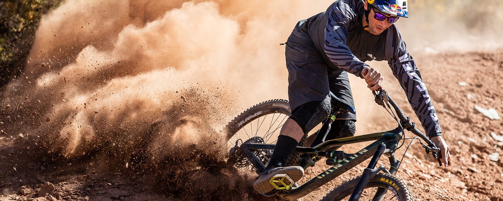 Person fährt Mountainbike durch staubige Kurve, trägt Helm und Brille. Actionaufnahme für Outdoor-Enthusiasten.