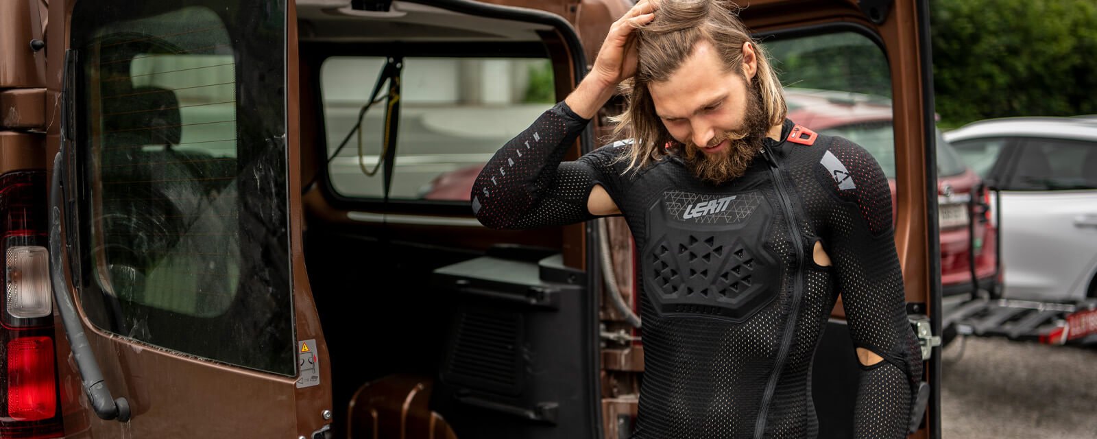 Mann trägt Leatt Protektorenhemd, steht neben offenem Lieferwagen, geeignet für Motorrad- oder Radfahrer.