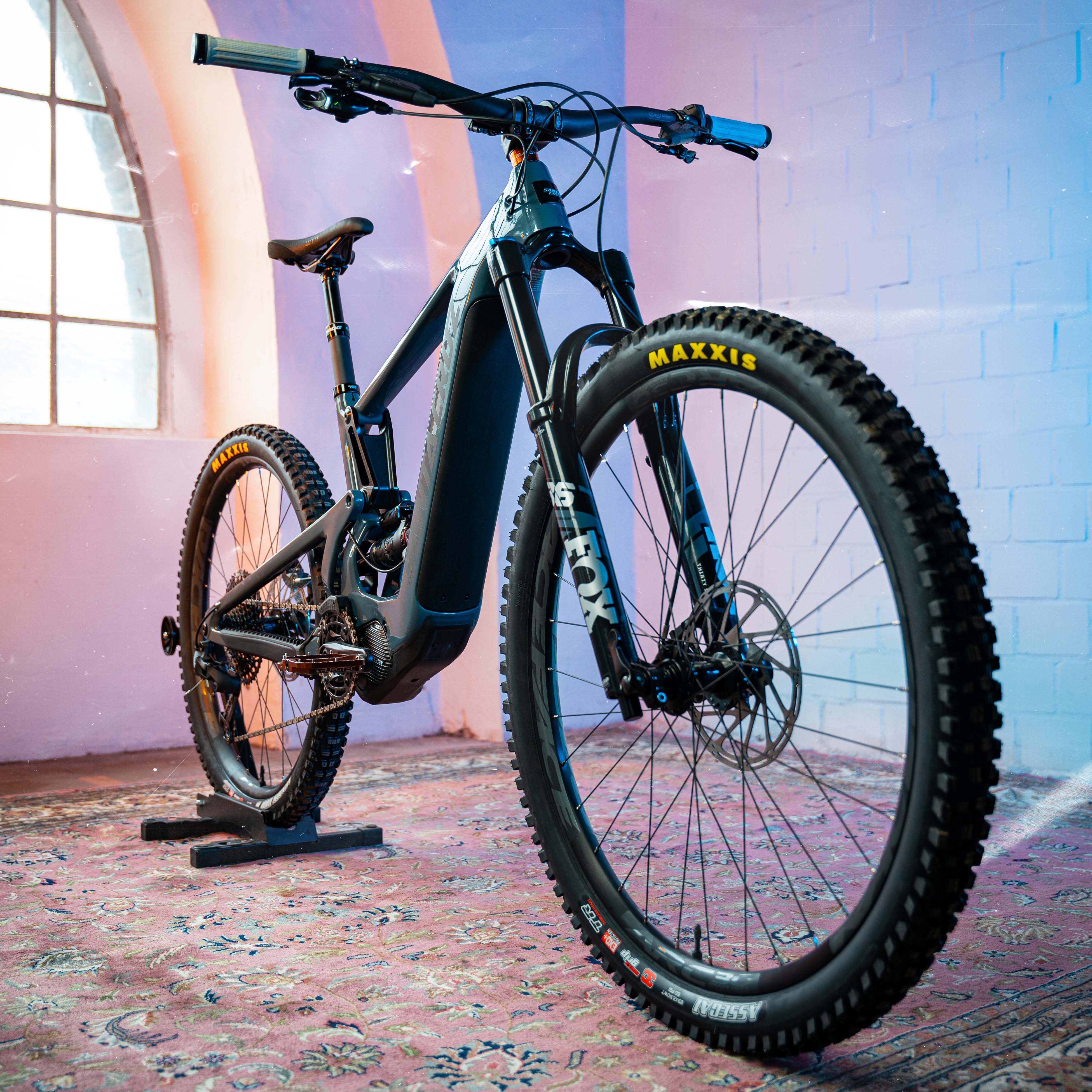 Santa Cruz Heckler E-Mountainbike mit Maxxis-Reifen, geeignet für anspruchsvolle Offroad-Touren in einem stilvollen Raum.