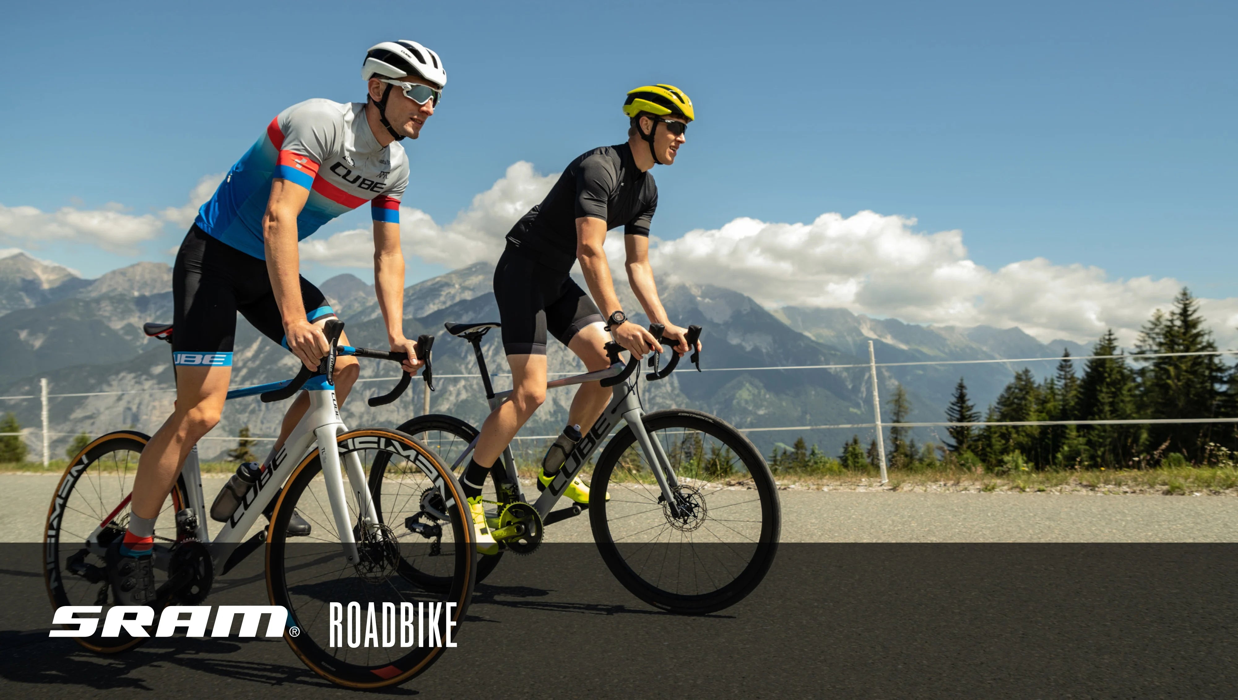 Zwei Radfahrer mit CUBE Rennrädern und SRAM Ausstattung fahren auf einer Bergstraße in sonniger Landschaft.