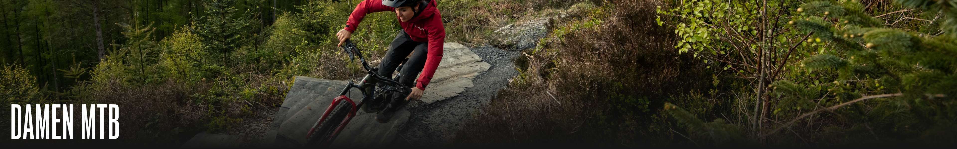Frau in roter Jacke fährt Mountainbike auf Waldpfad, Beschriftung "Damen MTB".