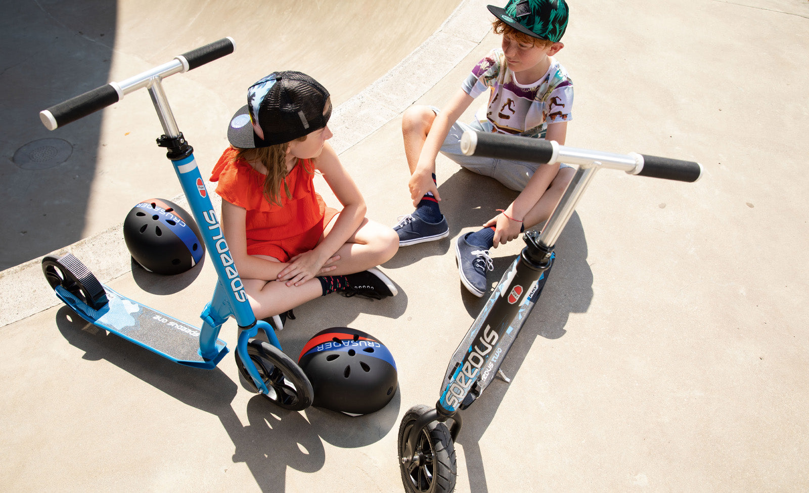 Zwei Kinder mit Helmen sitzen neben "Scoot and Ride" Rollern; geeignet für Outdoor-Abenteuer.