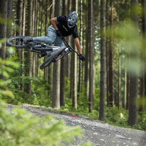 Mountainbiker springt mit Cube Two15 durch bewaldeten Trail. Ideal für Downhill-Liebhaber.