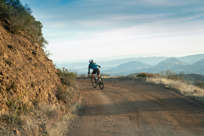 Radfahrer auf einer Schotterstraße in hügeliger Landschaft, ideal für Offroad-Abenteuer mit dem Specialized Gravel-Bike.
