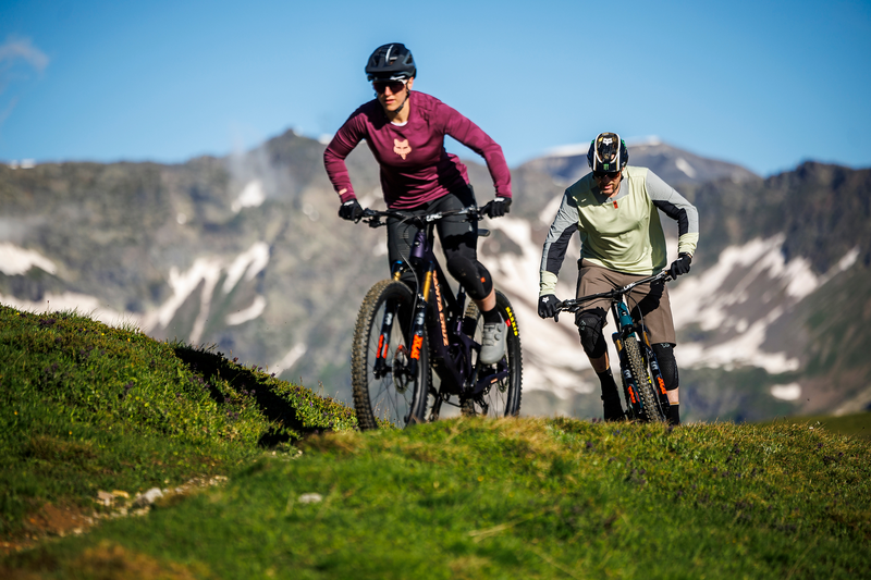 Zwei Mountainbiker fahren Santa Cruz Hightower Fahrräder auf einem grasbewachsenen Hügel in alpiner Landschaft.