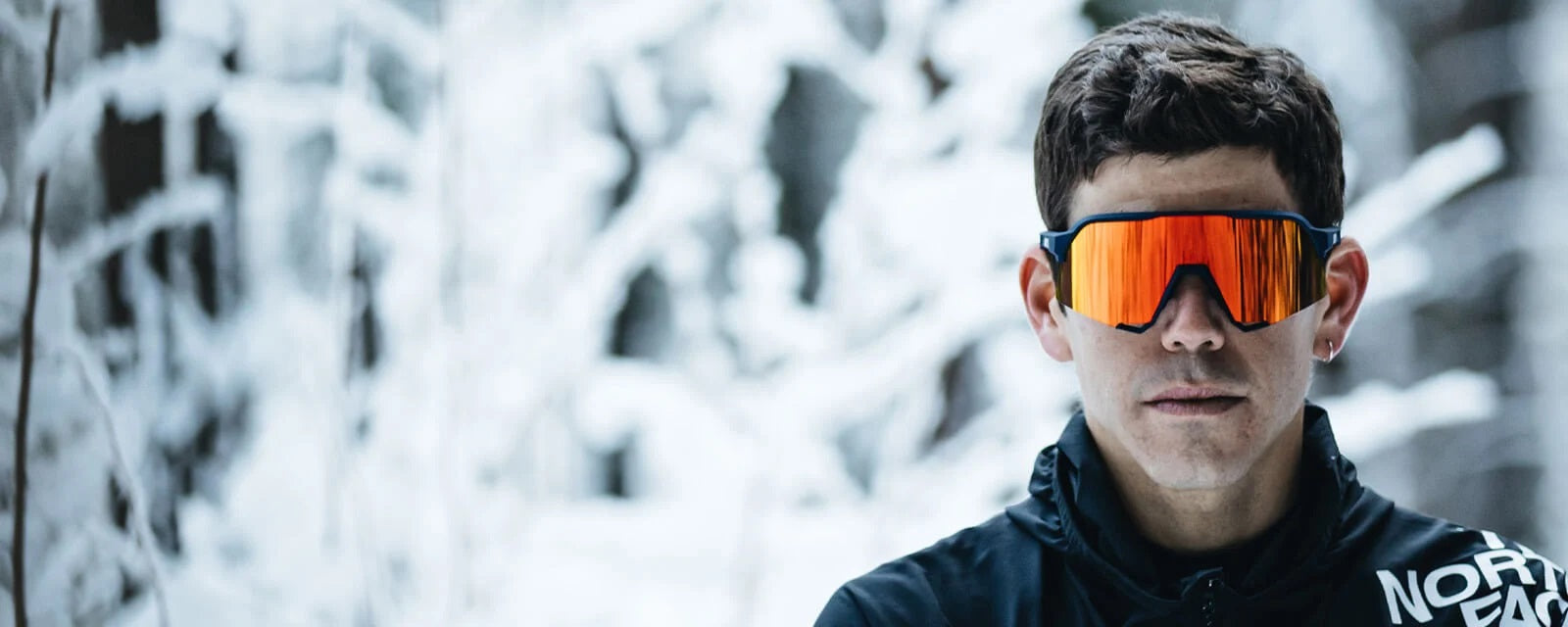 Person im Schnee trägt sportliche, orange verspiegelte Sonnenbrille. Geeignet für Outdoor-Aktivitäten im Winter.
