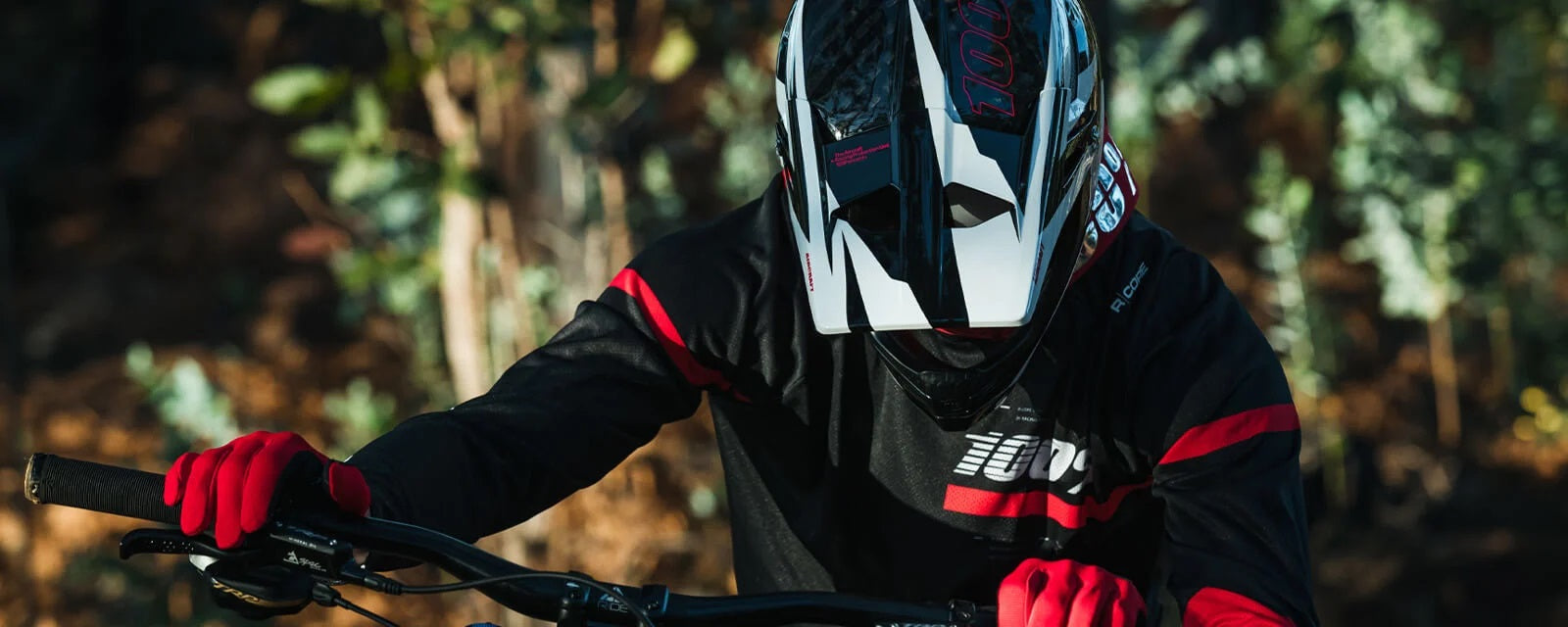 Mountainbike-Fahrer mit 100% Helm und Handschuhen radelt durch bewaldetes Gebiet.