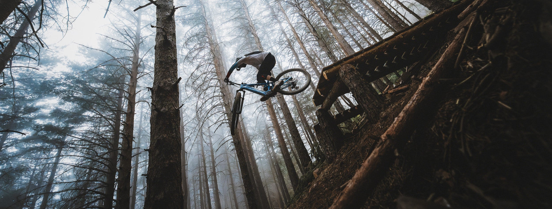 Mountainbiker springt im Wald über einen Holzsteg mit einem Mondraker Sly Bike.