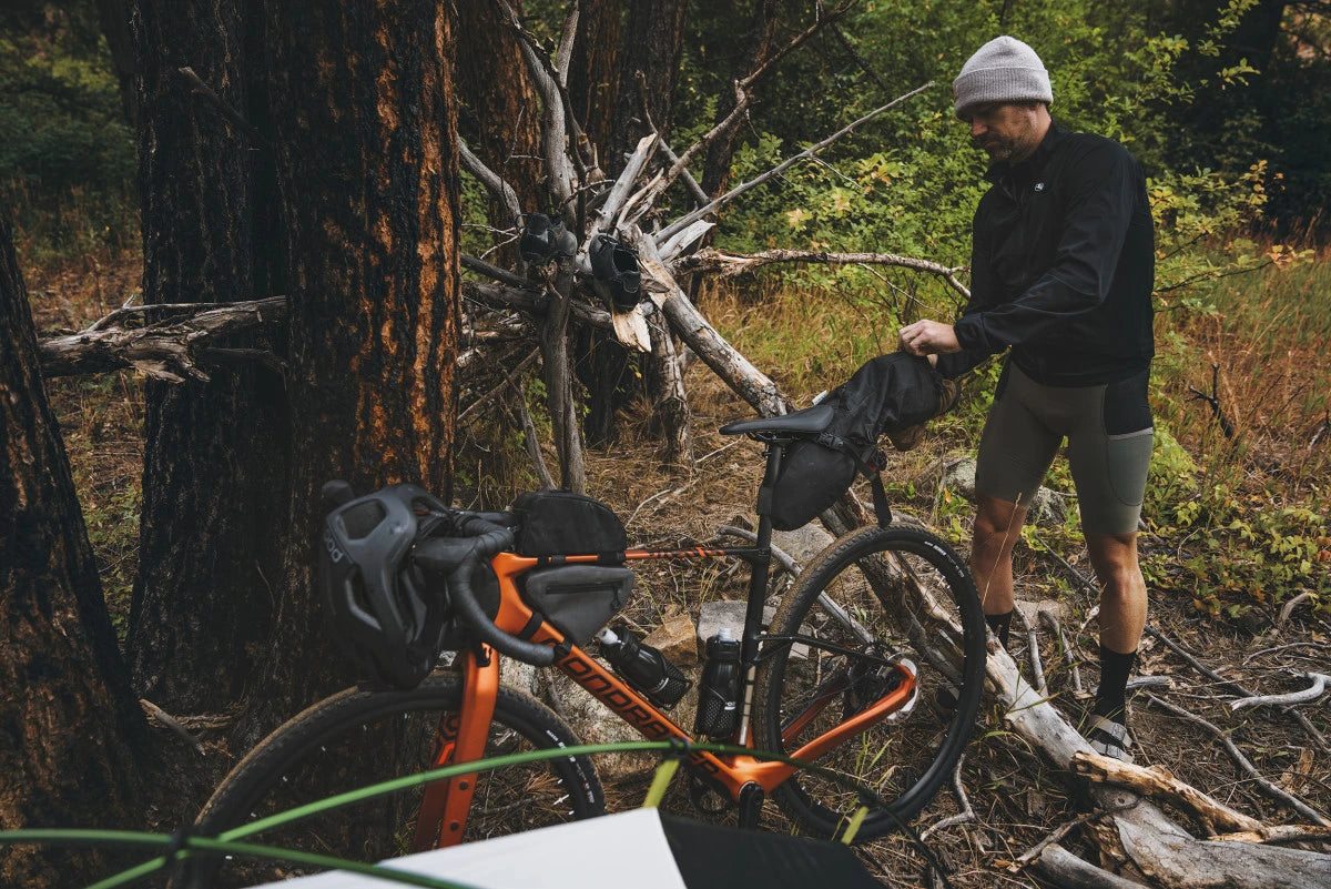 Mann packt Mondraker Arid Fahrrad in Waldumgebung, ideal für Gelände- und Abenteuerradfahren.