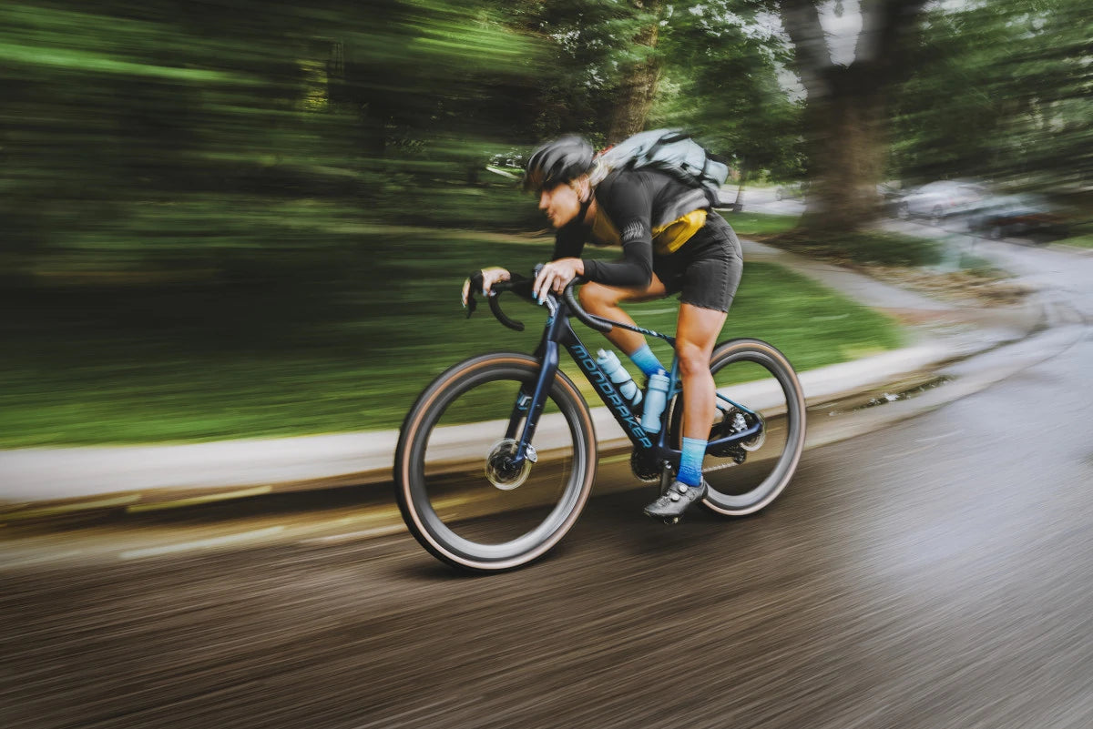 Person auf Mondraker Rennrad, fährt schnell auf nasser Straße, trägt Helm und Rucksack.
