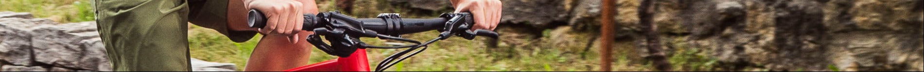 Nahaufnahme eines Fahrradlenkers mit rotem Rahmen, gehalten von einer Person in grüner Hose, BMC Alpenchallenge-Modell.