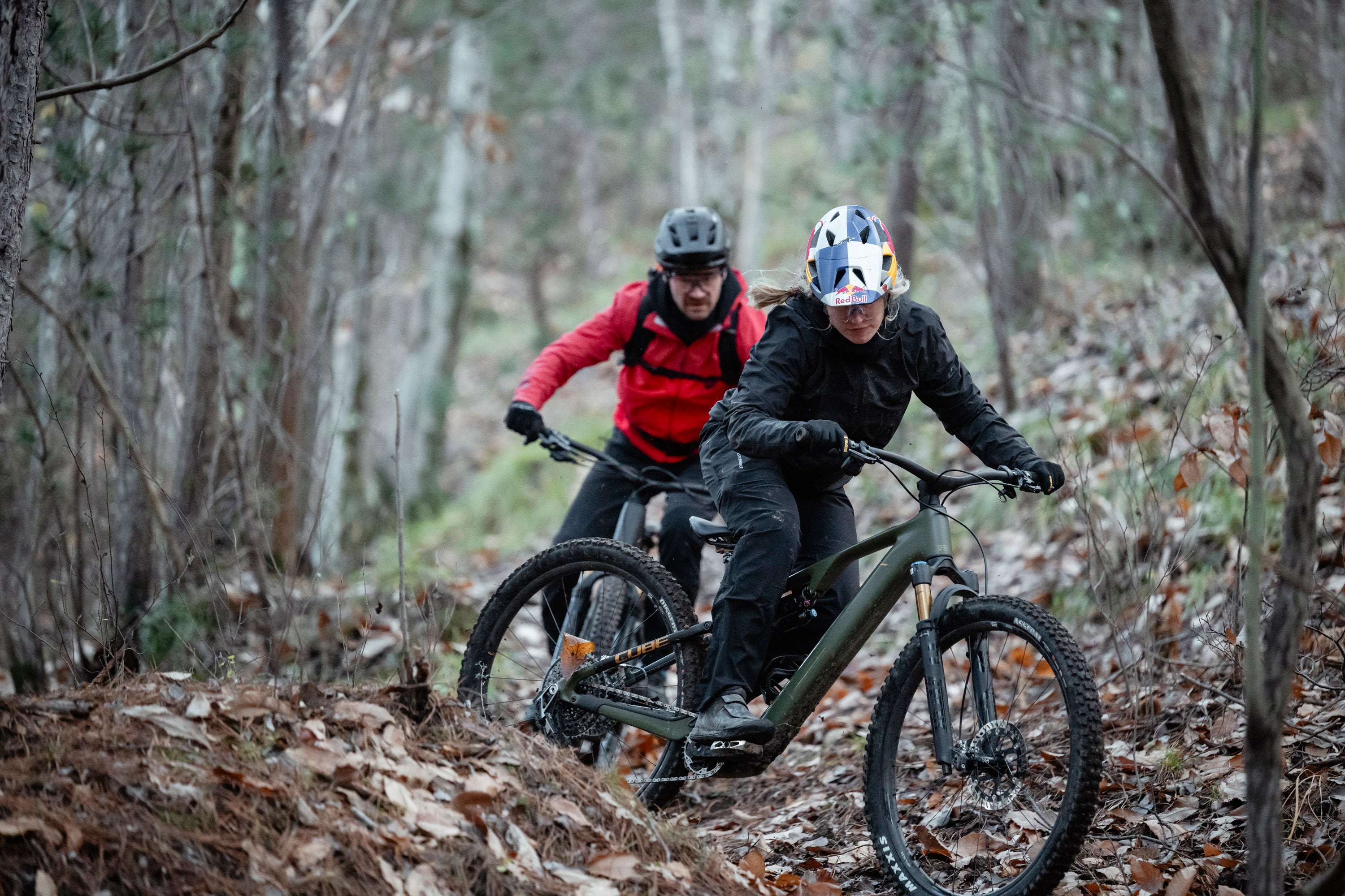 Zwei Mountainbiker fahren auf CUBE-Rädern im Wald. Sie tragen Schutzkleidung und Helme.