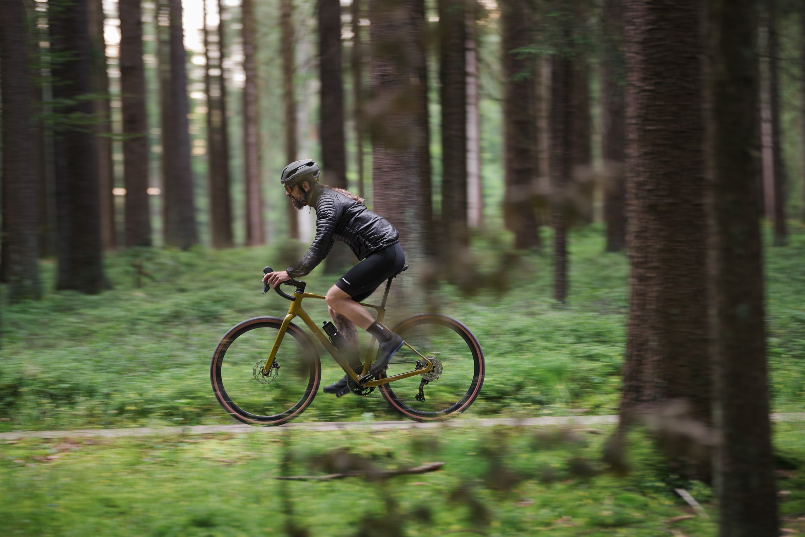 Radfahrer auf einem goldenen Gravelbike im Wald, ideal für Outdoor-Enthusiasten, Modell aus der Kollektion Cube 2025.