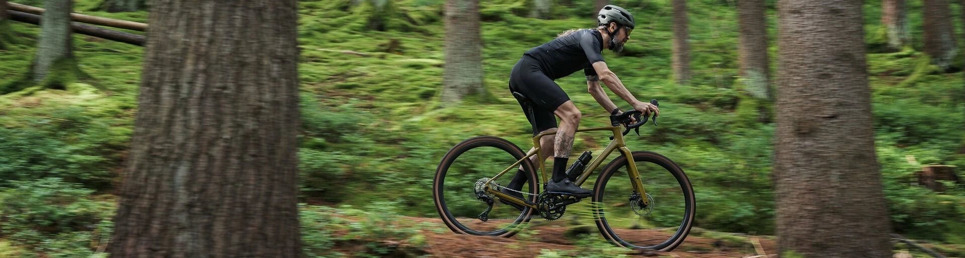 Radsportler auf Cube-Gravelbike im Wald, dynamische Fahrt durch grünes Gelände. Ideal für Offroad-Abenteuer.