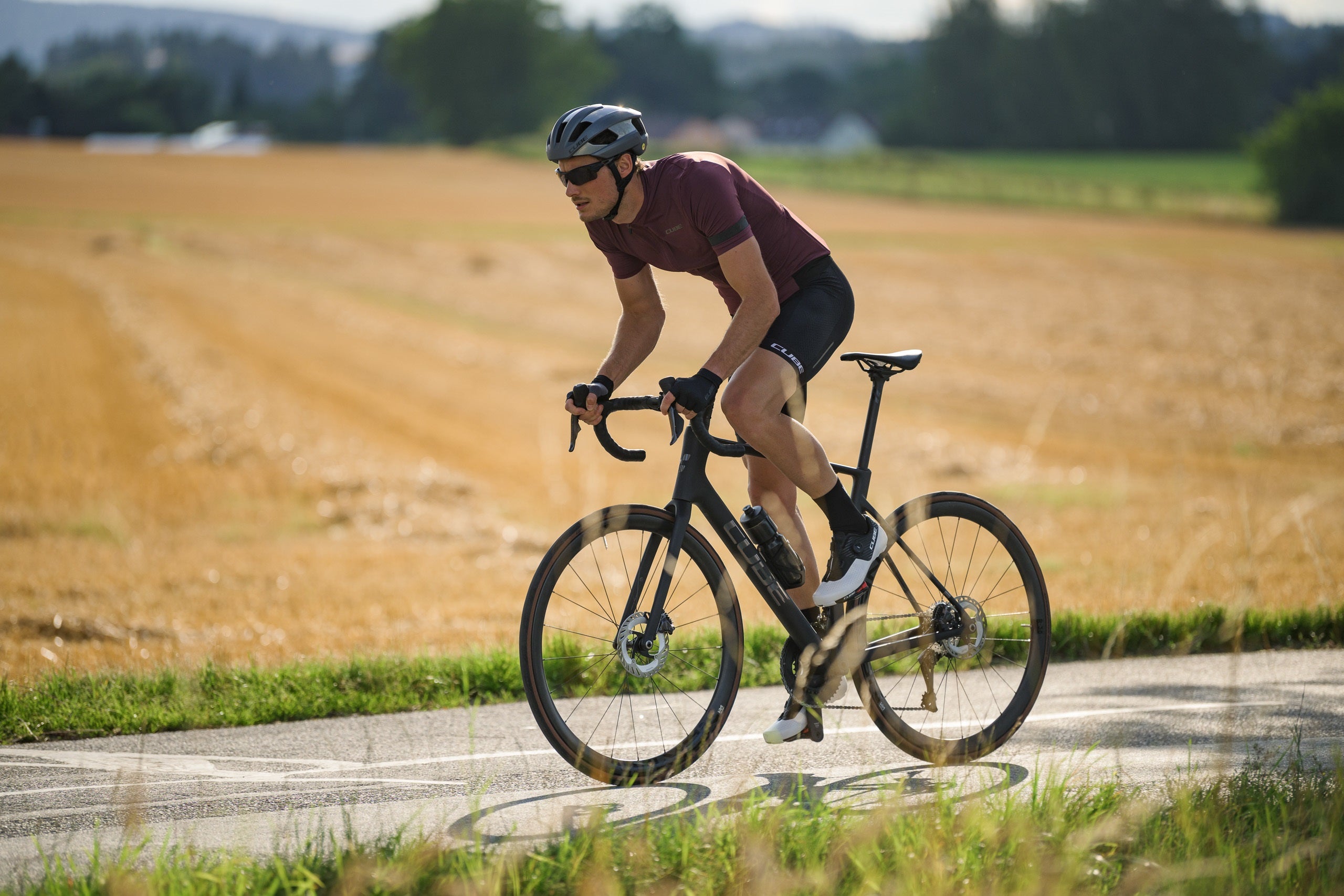 Radfahrer auf Cube-Rennrad in Sommerlandschaft, geeignet für sportliche Straßenfahrten; Collection Cube Neuheiten 2025.