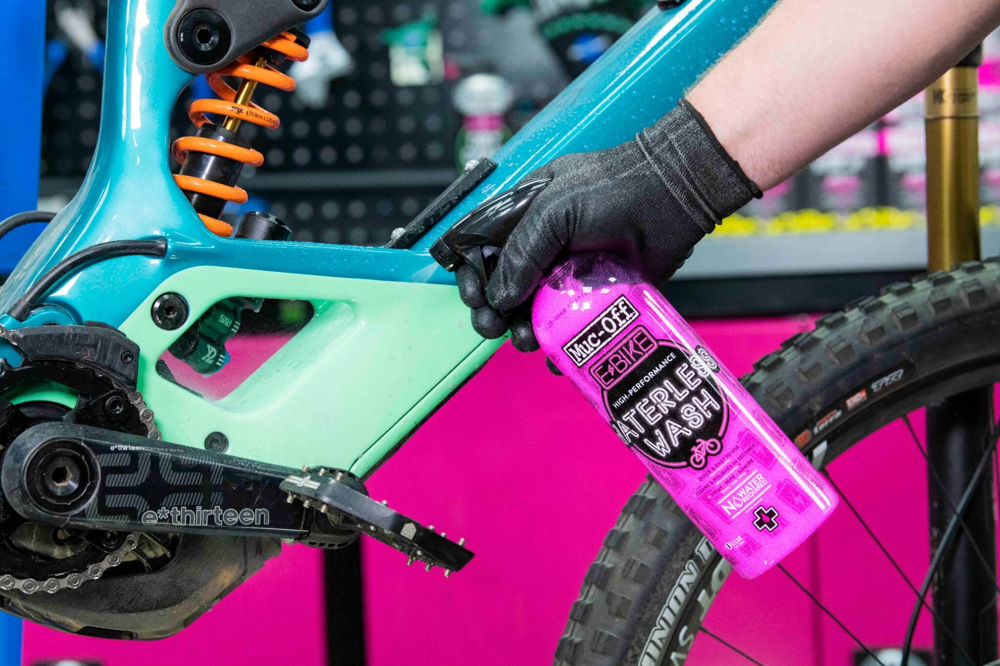 Hand sprüht Muc-Off E-Bike Waterless Wash auf türkisfarbenes Fahrrad, geeignet zur schnellen Reinigung ohne Wasser.
