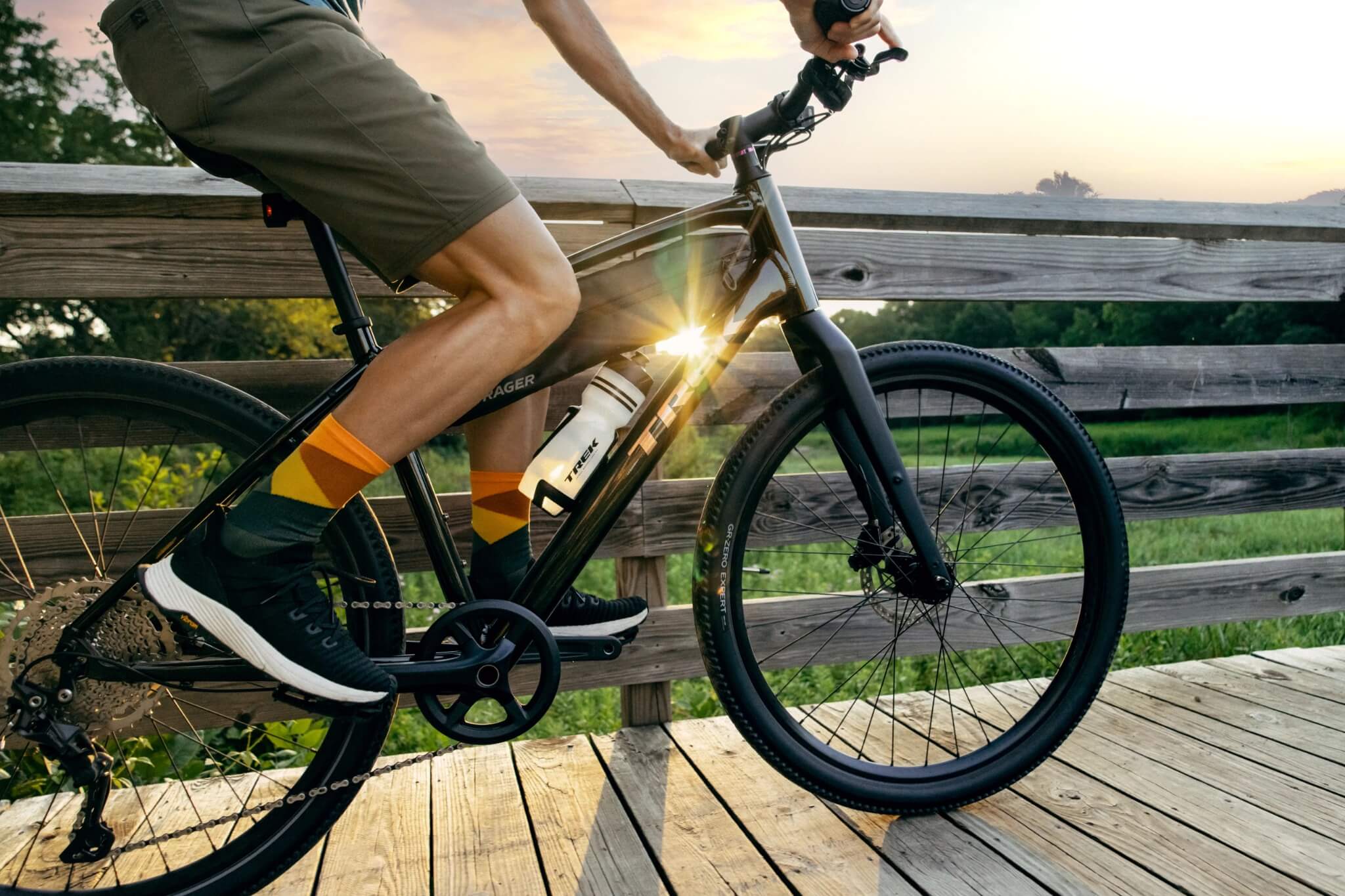 Person fährt bei Sonnenuntergang ein Trek Dual Sport Fahrrad auf einem Holzweg, geeignet für Outdoor-Abenteuer.
