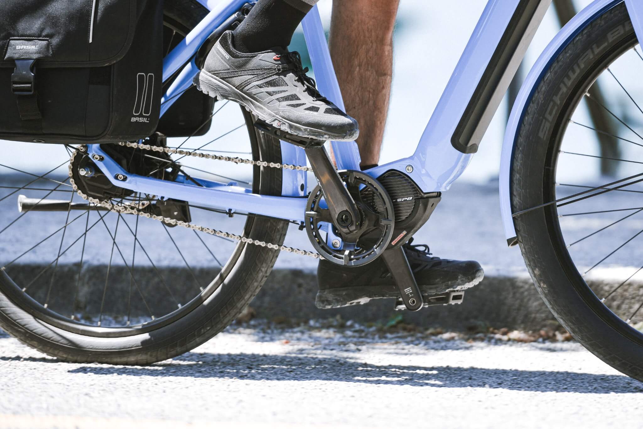E-Bike mit Schwalbe-Reifen und BASIL Fahrradtasche, ideal für City-Trekking, Nahaufnahme des Tretlagers und Kettenantriebs.