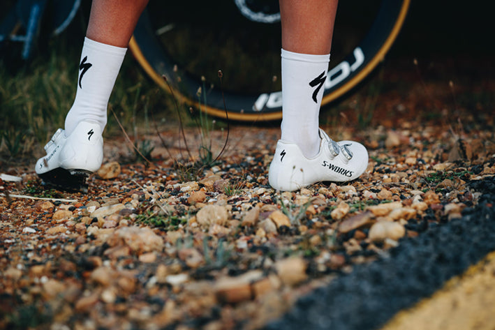 Weiße Specialized S-Works Fahrradschuhe und Socken auf Schotter, passend für Radsport-Profis oder Amateure.