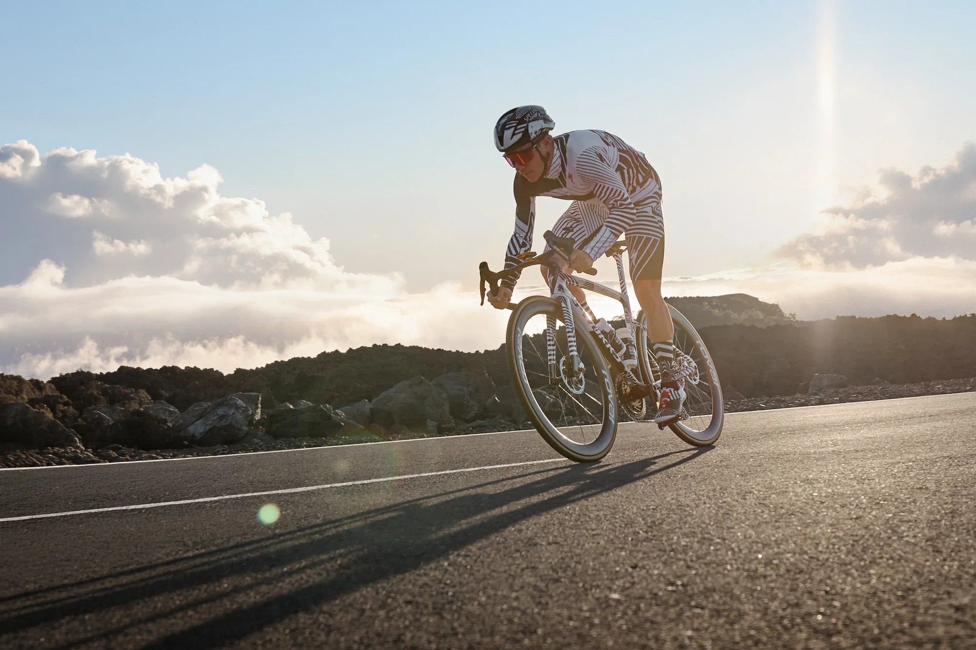 Radfahrer in Zebra-Trikot auf einer Straße bei Sonnenuntergang, fährt ein Specialized Tarmac SL9 S-Works - Ideal für sportliche Radtouren.
