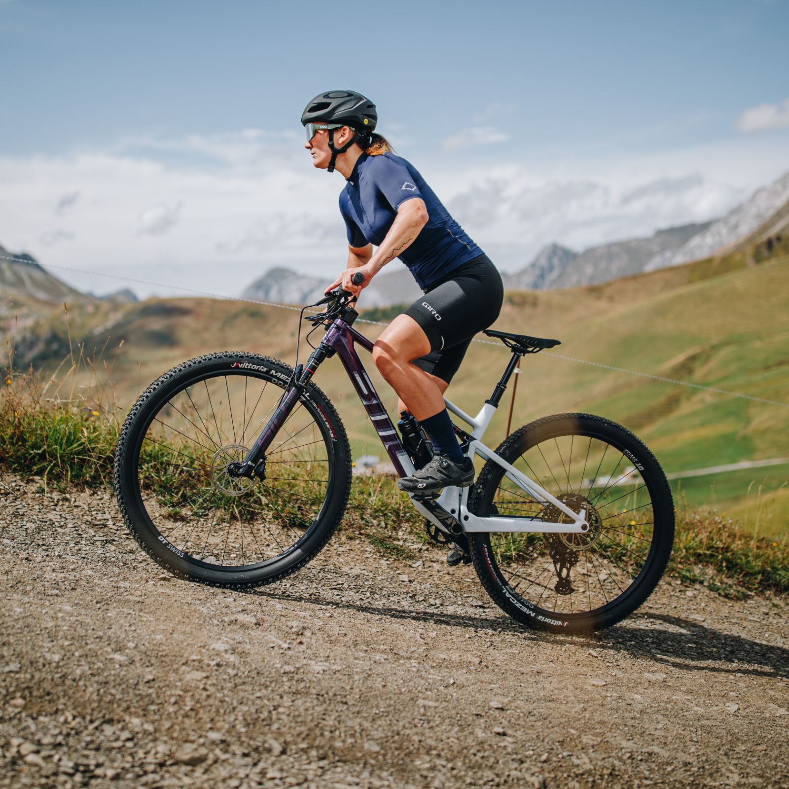 Frau auf Mountainbike von Scott, Modell Spark, fährt auf Schotterweg in bergiger Landschaft mit Helm und Sportkleidung.