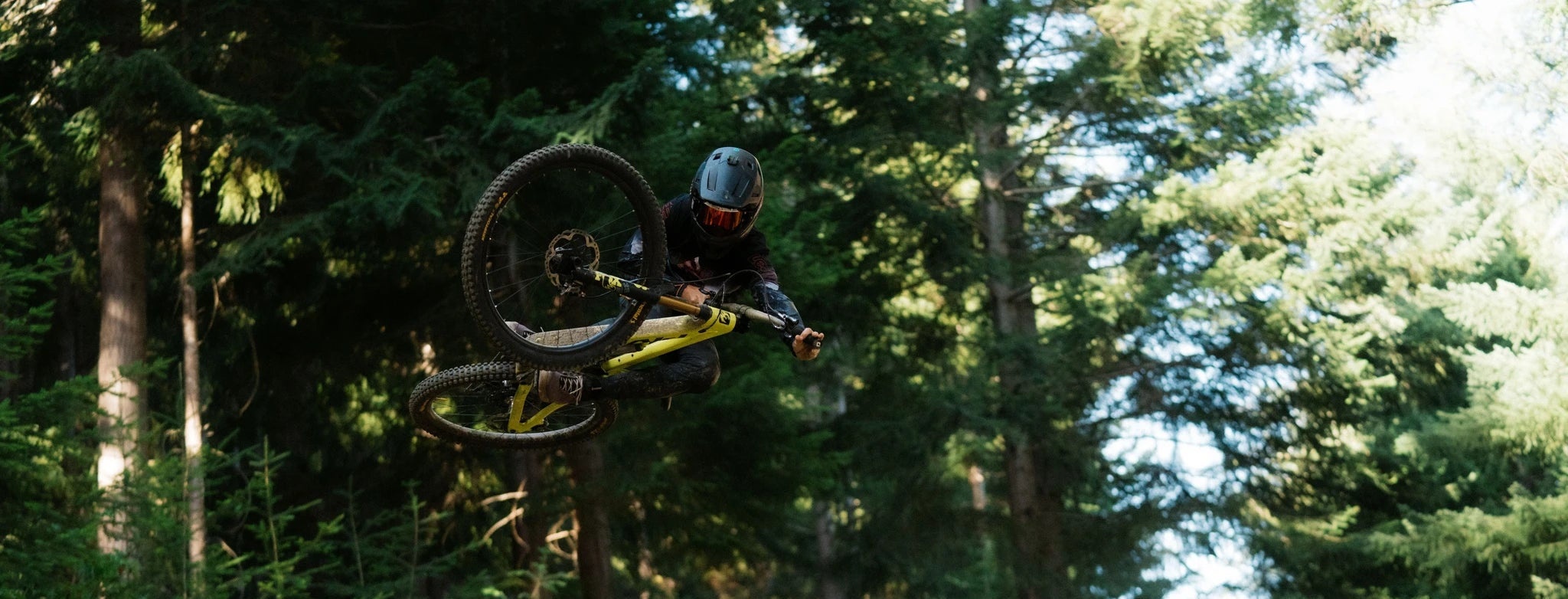 Fahrradfahrer in der Luft mit gelbem Mountainbike im Wald; Helm und Schutzkleidung, ideal für Freeride-Enthusiasten.